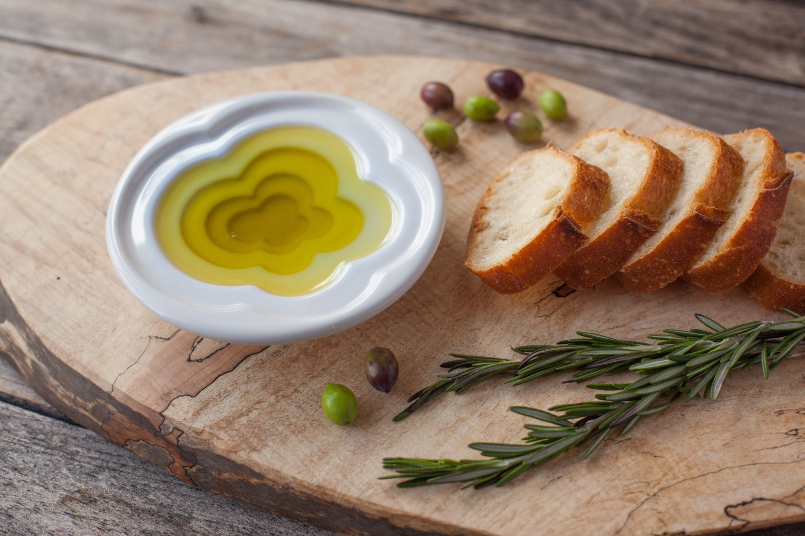 Olive oil served on a wooden plade with rosemary and small bread